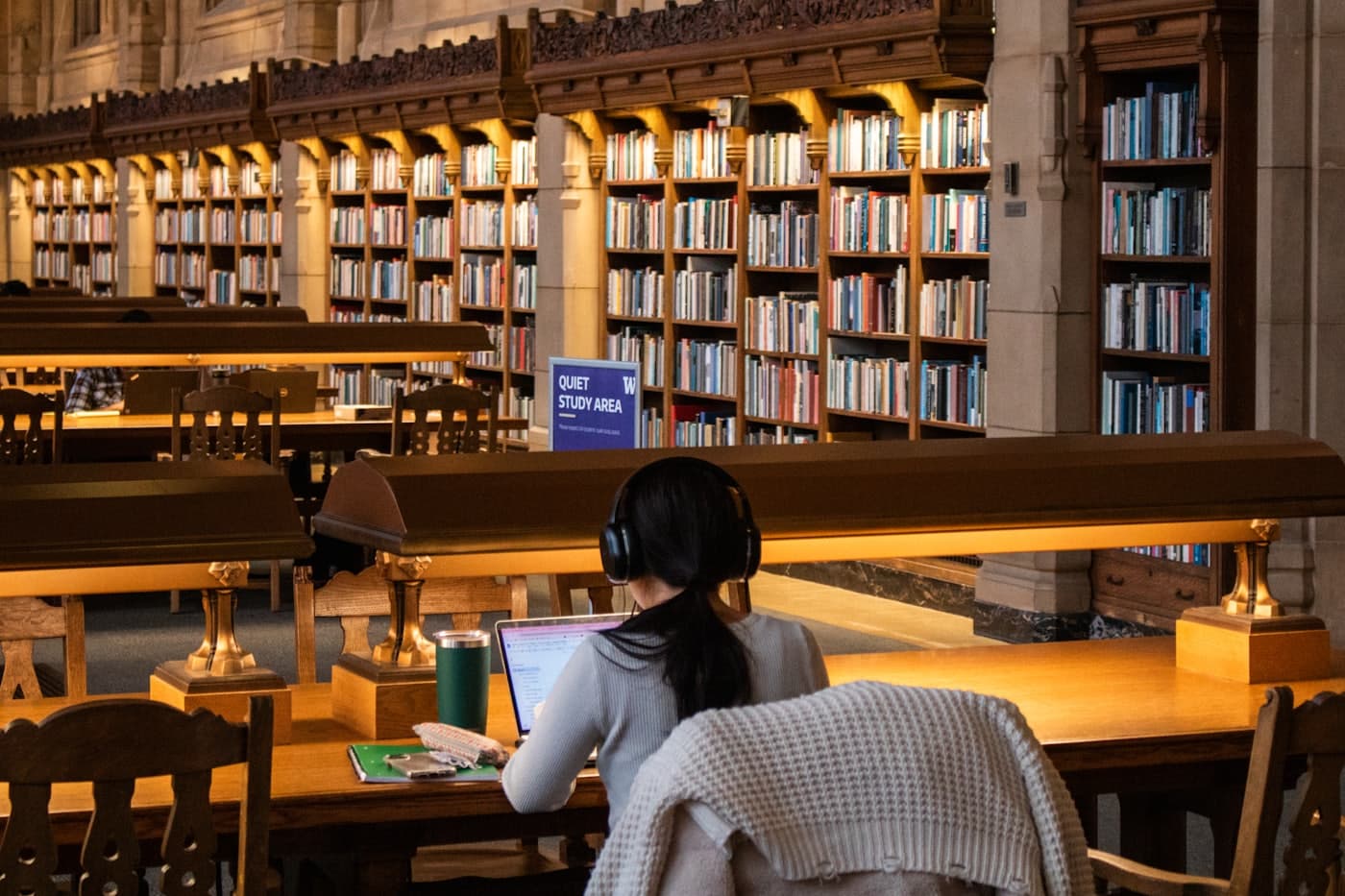 A student working at a long desk in a wood-panelled library lined with bookshelves