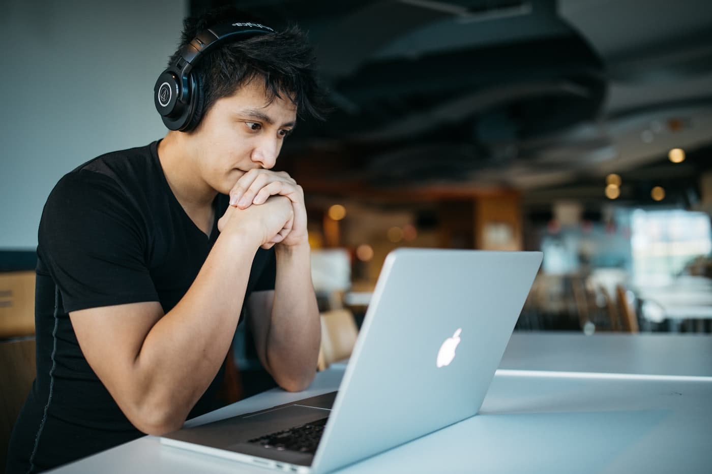A student concentrating on a laptop screen with headphones on, in a bright study space